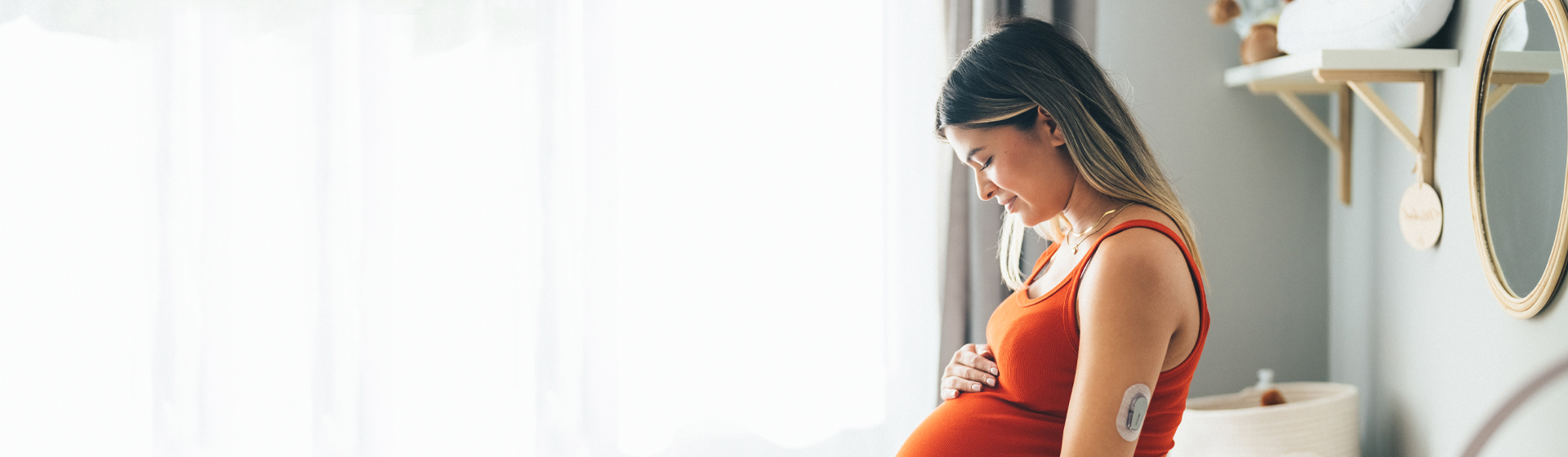 Pregnant woman wearing a CGM holds her belly