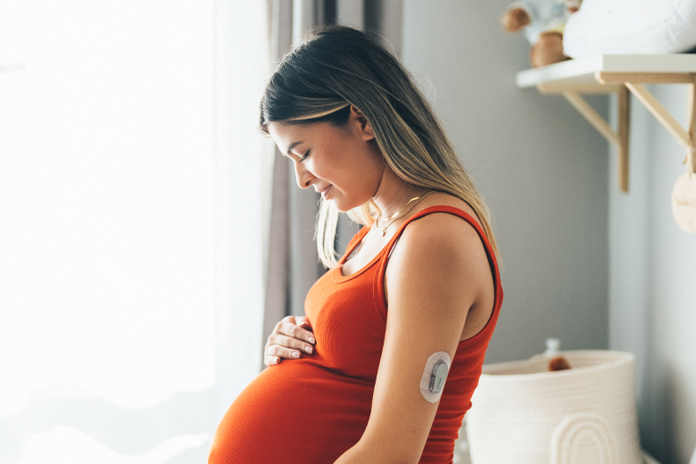 Pregnant woman wearing a CGM holds her belly